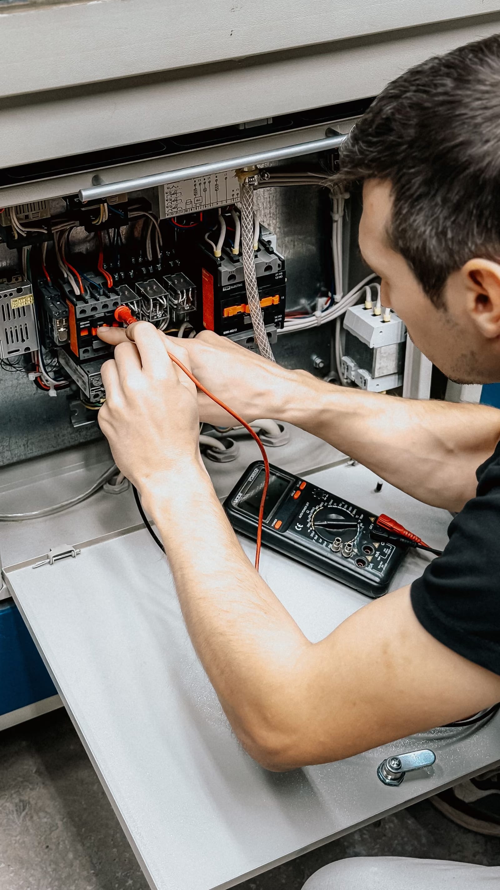 Elektrikář měří zapojení v otevřeném rozvaděči.